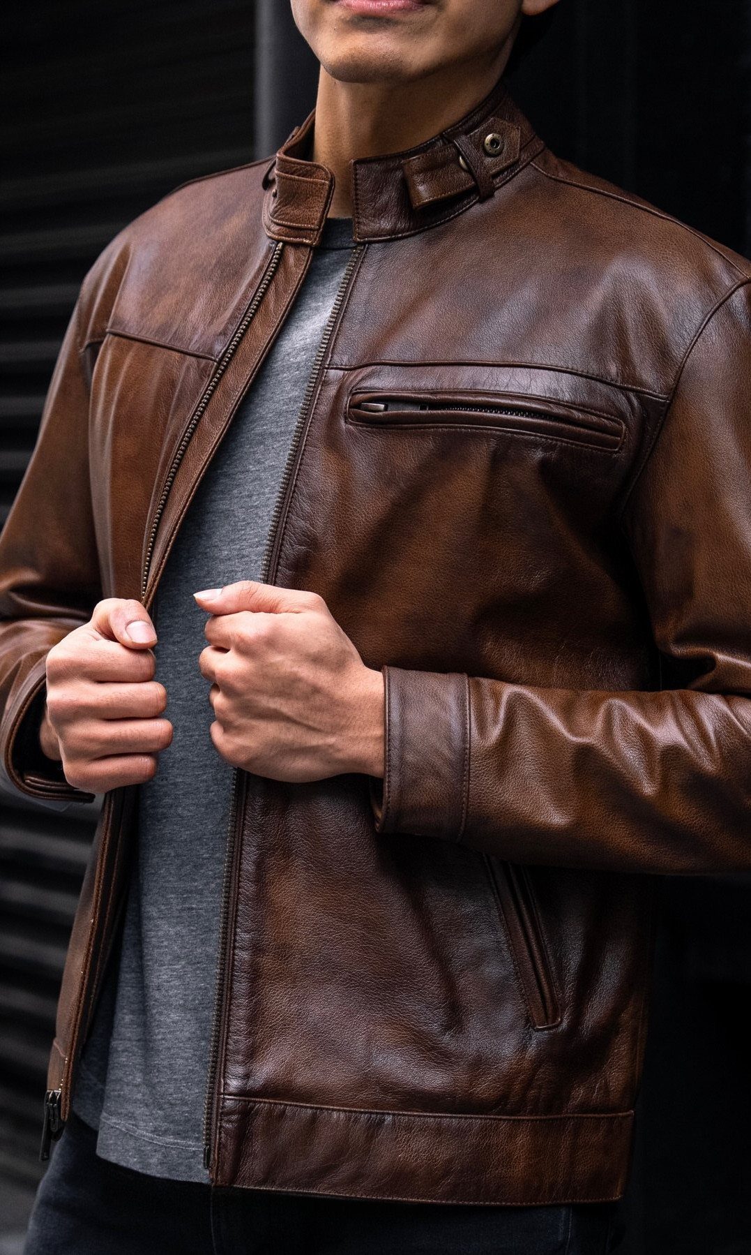 Brown leather jacket worn over a grey t-shirt against a dark background