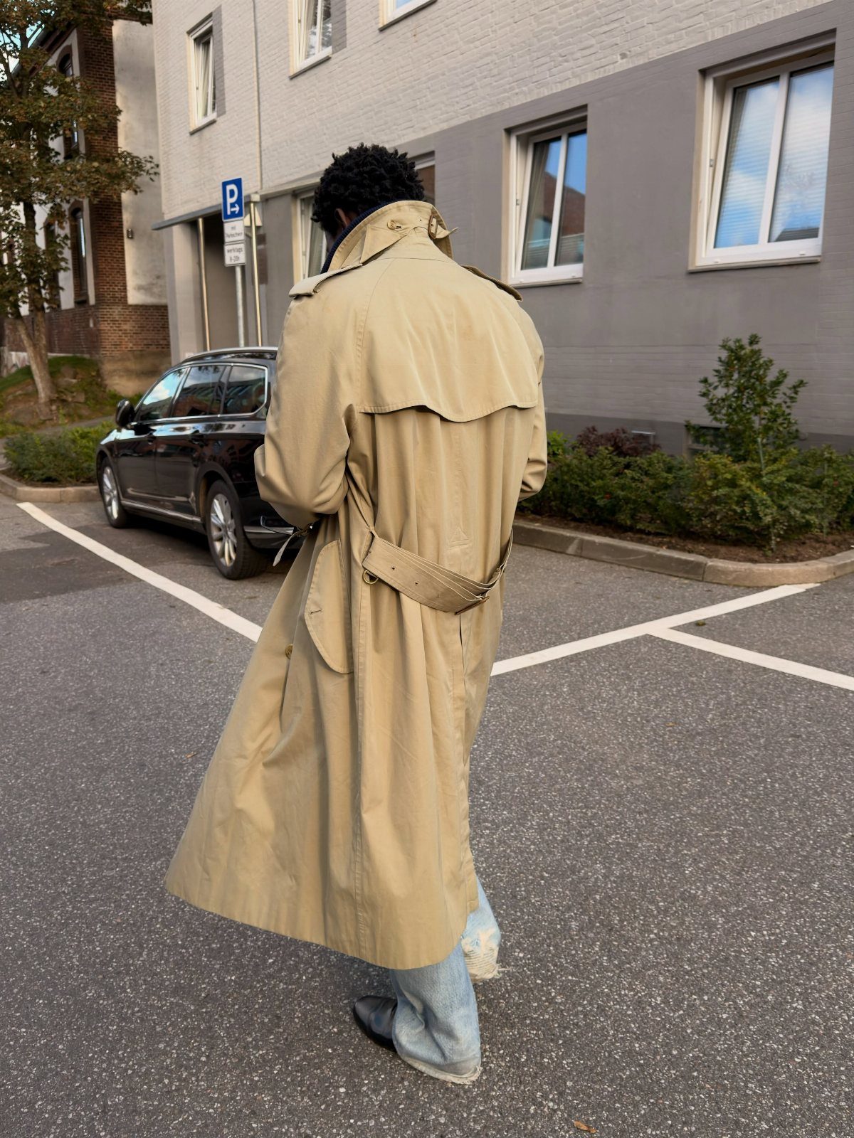 Person from behind wearing a tan knee-length trench coat and light blue jeans.