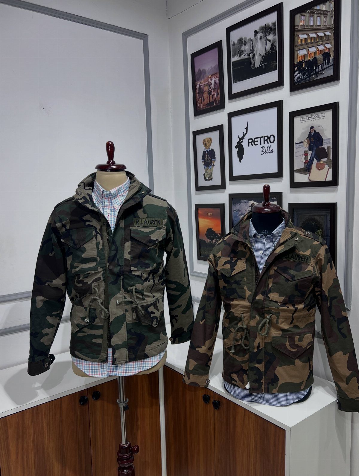 Two camouflage jackets on mannequins displayed in a store with framed wall art.