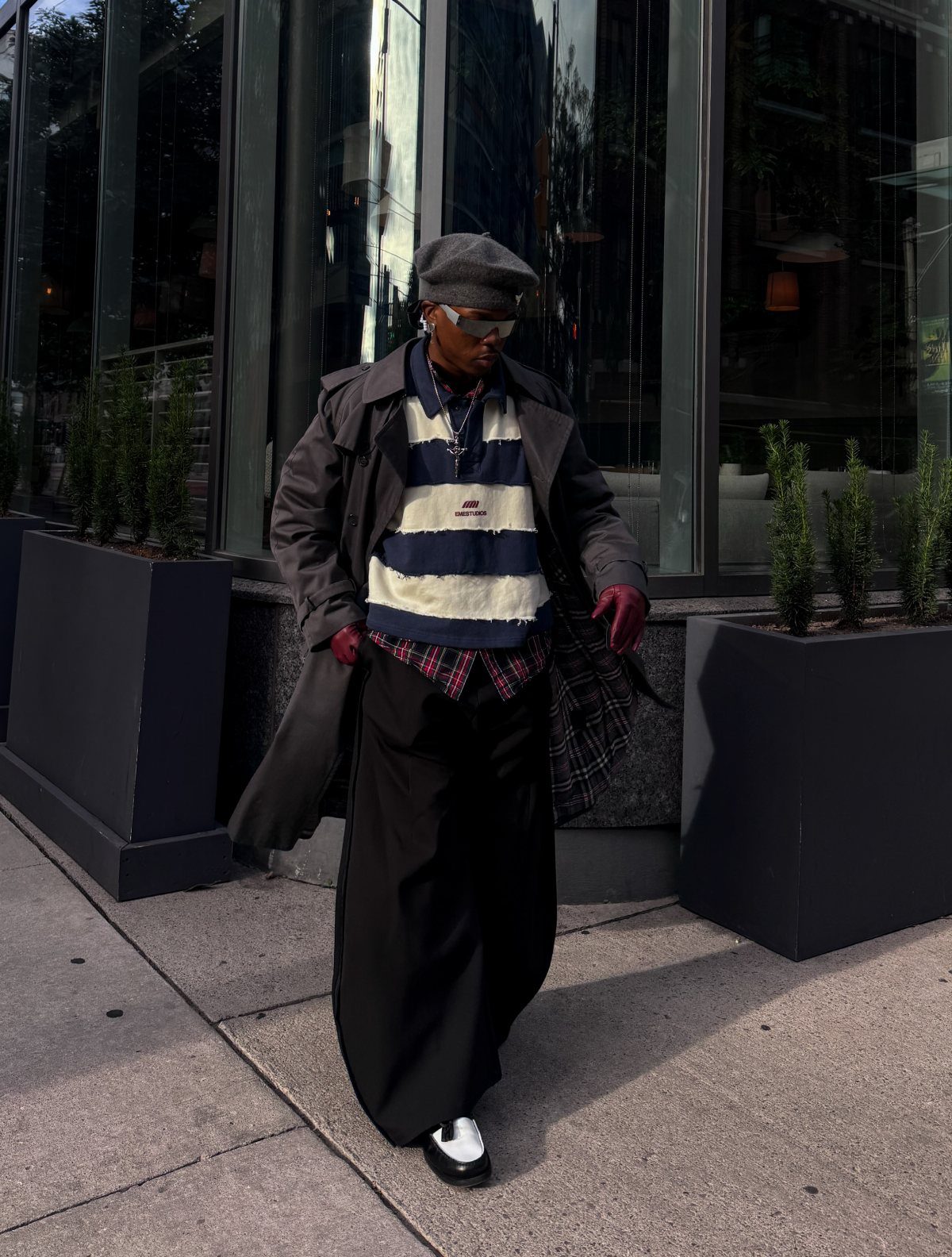 Person wearing a long dark coat over a striped shirt and wide trousers.