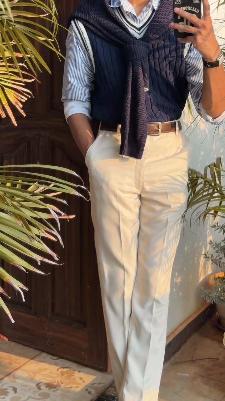 Man wearing a striped shirt, cream trousers, and navy sweater draped over shoulders.