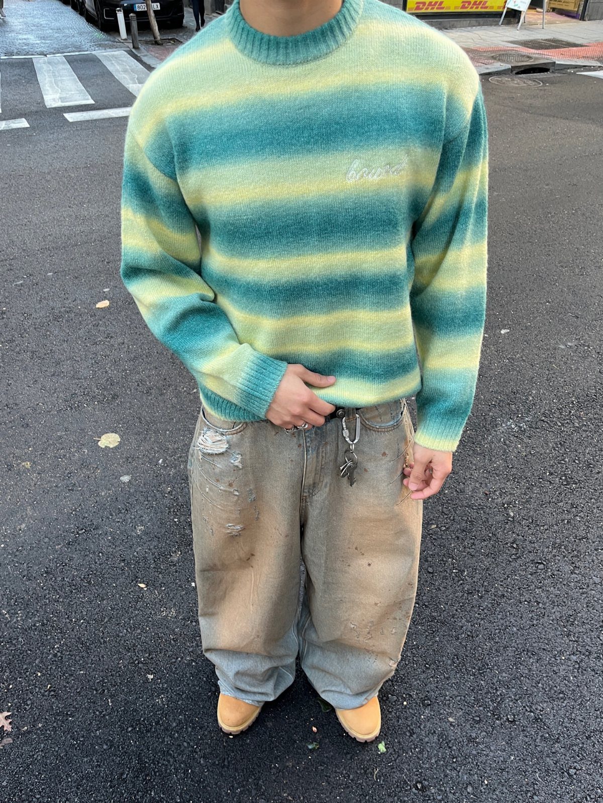 Person wearing a striped sweater and baggy distressed light-wash denim pants on street.