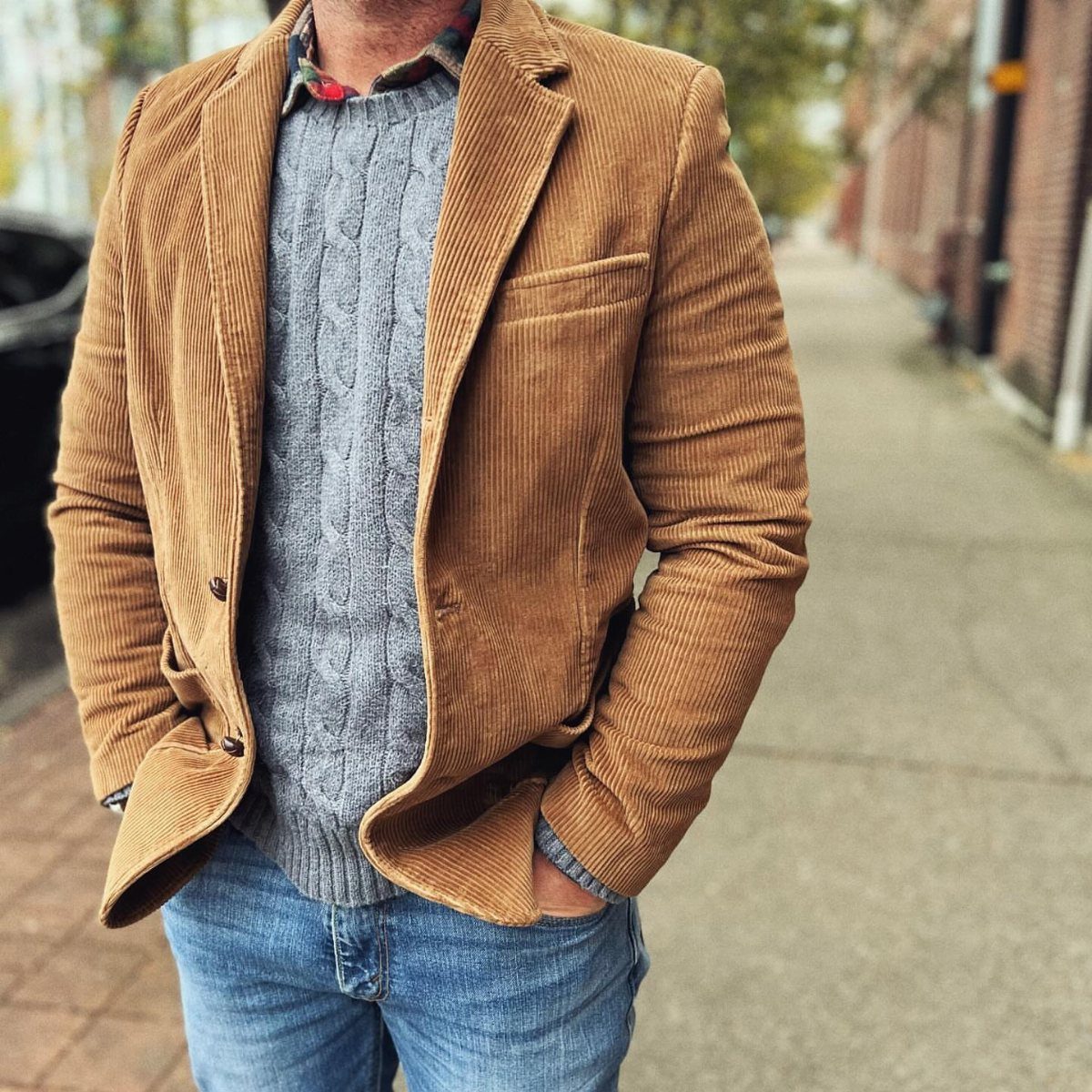 Brown corduroy blazer worn over a grey cable-knit sweater and blue jeans.