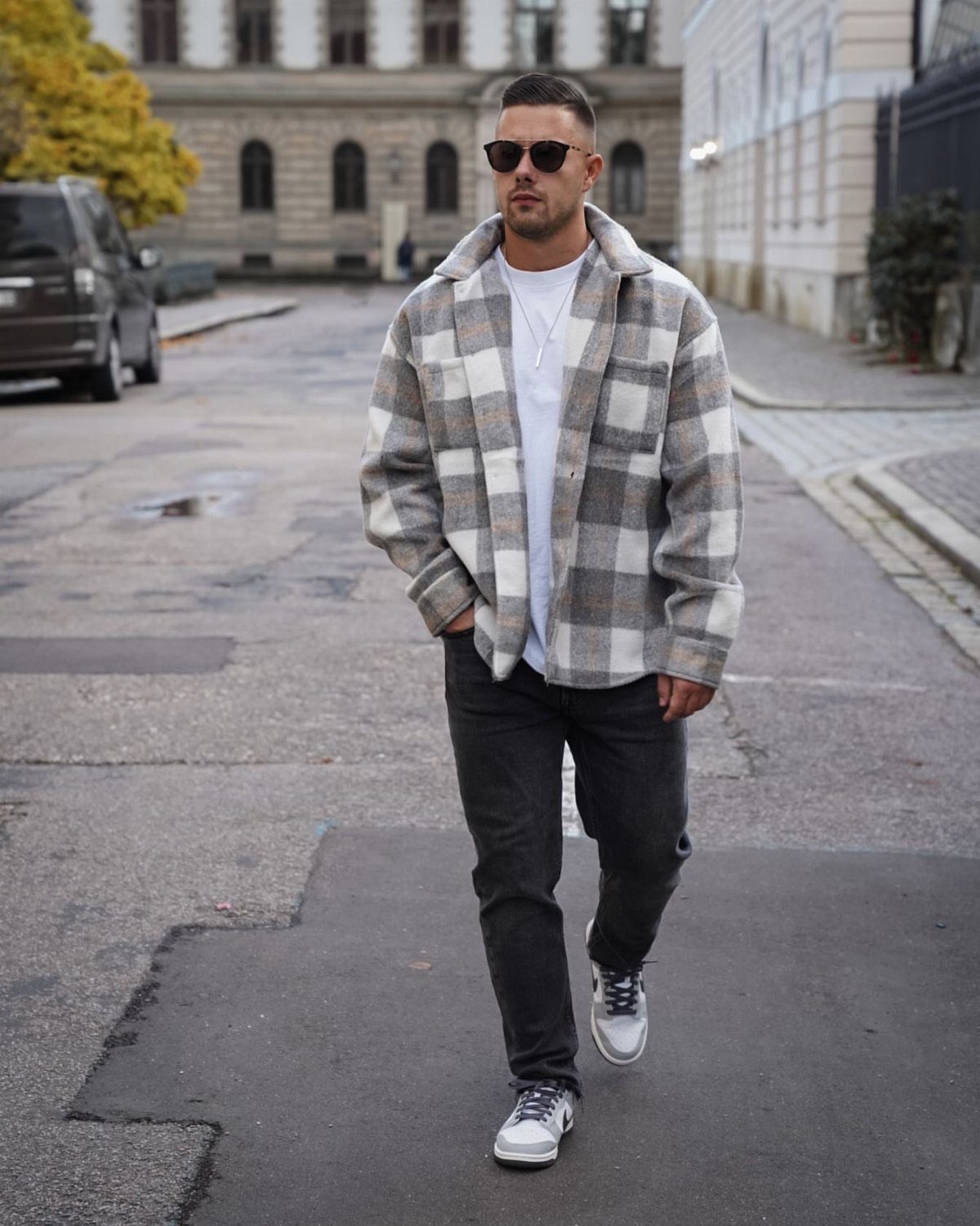 Man walking on a city street wearing a grey plaid flannel shirt and sneakers.