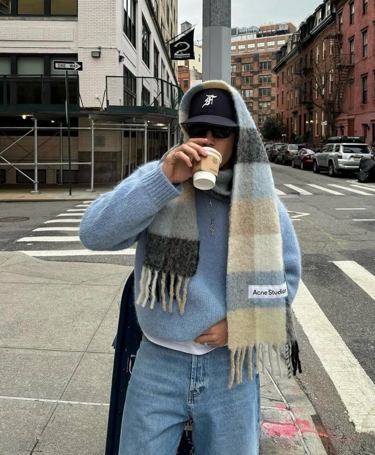 Person in a blue sweater wearing a long plaid scarf on a city street