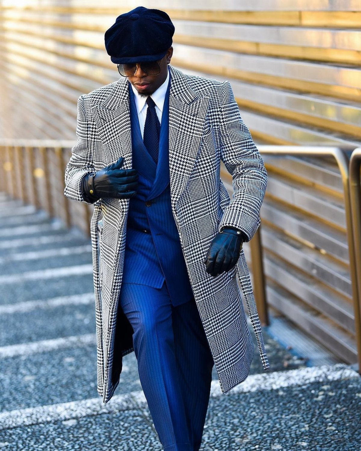 Man in a blue suit and grey houndstooth coat walking down stairs.
