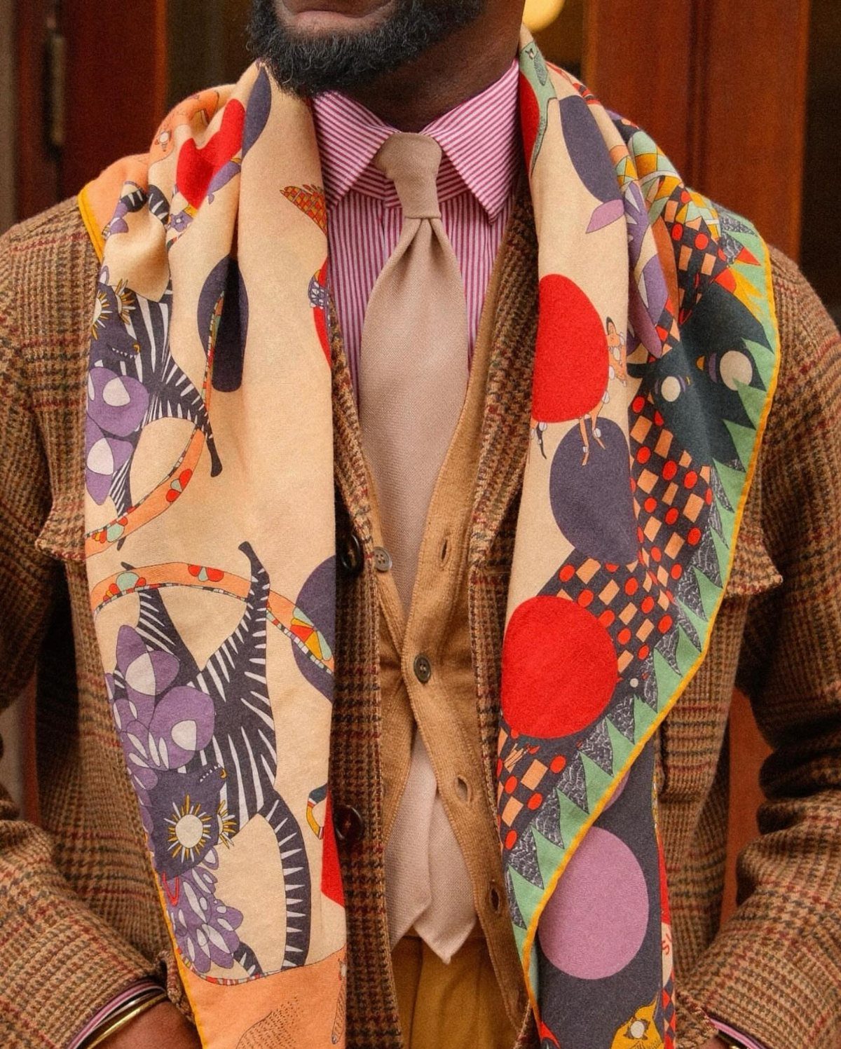 Man wearing a brown blazer and a beige scarf with colorful abstract prints.