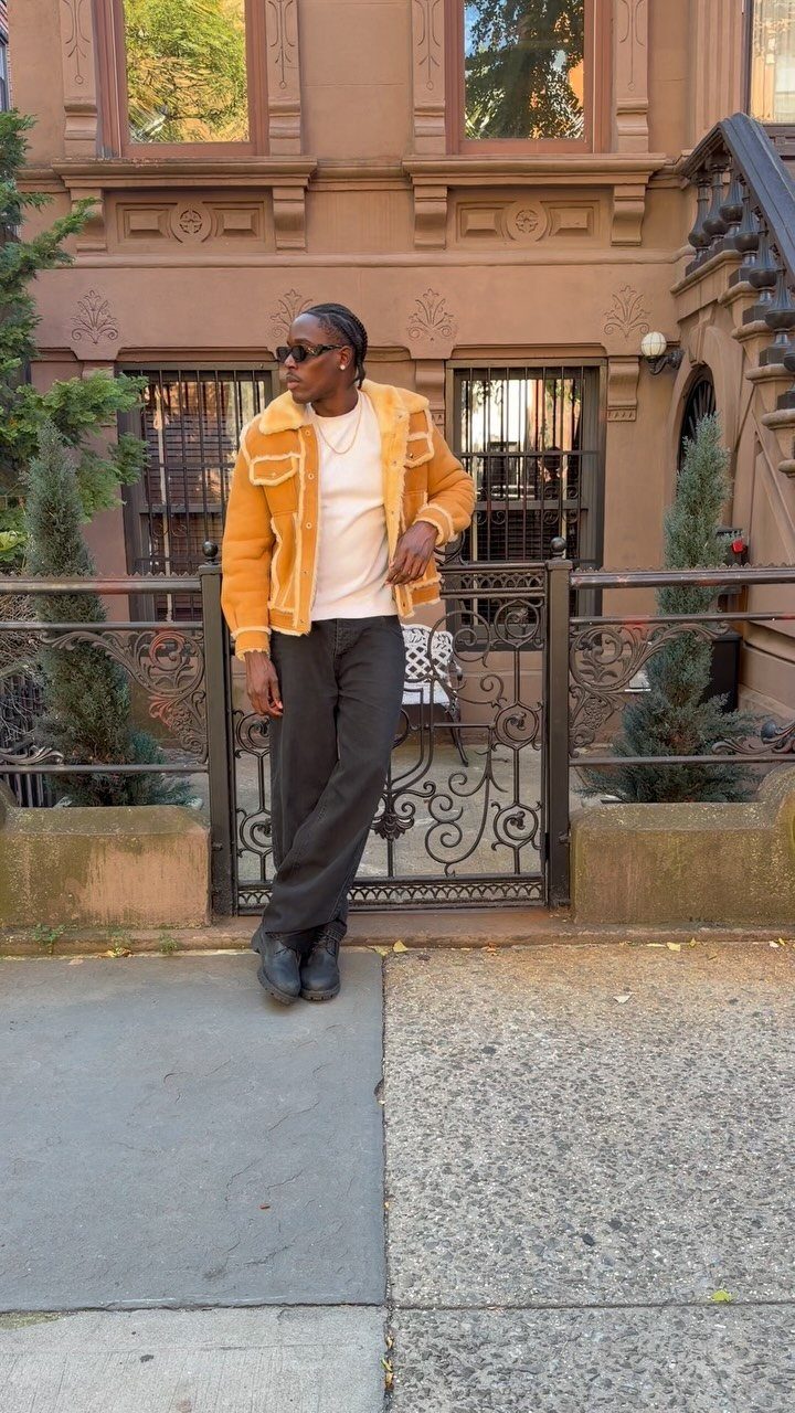 Person wearing a mustard yellow shearling jacket and baggy trousers outside a brownstone.