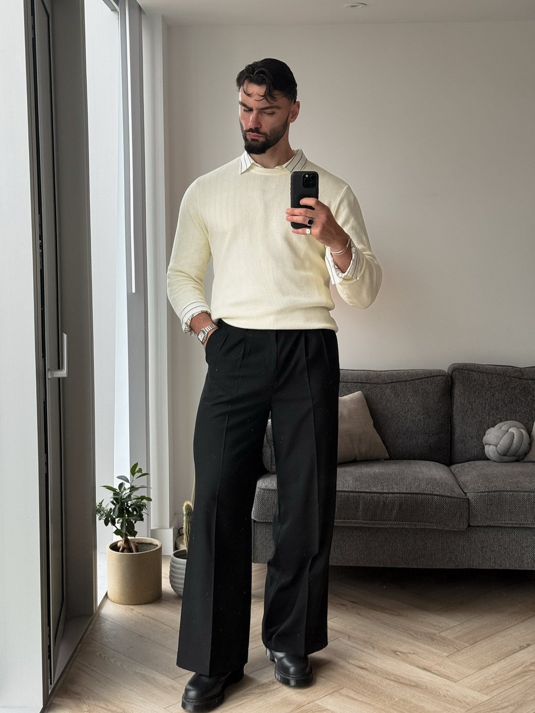 Man wearing a cream ribbed knit sweater and wide-leg black trousers in a room.
