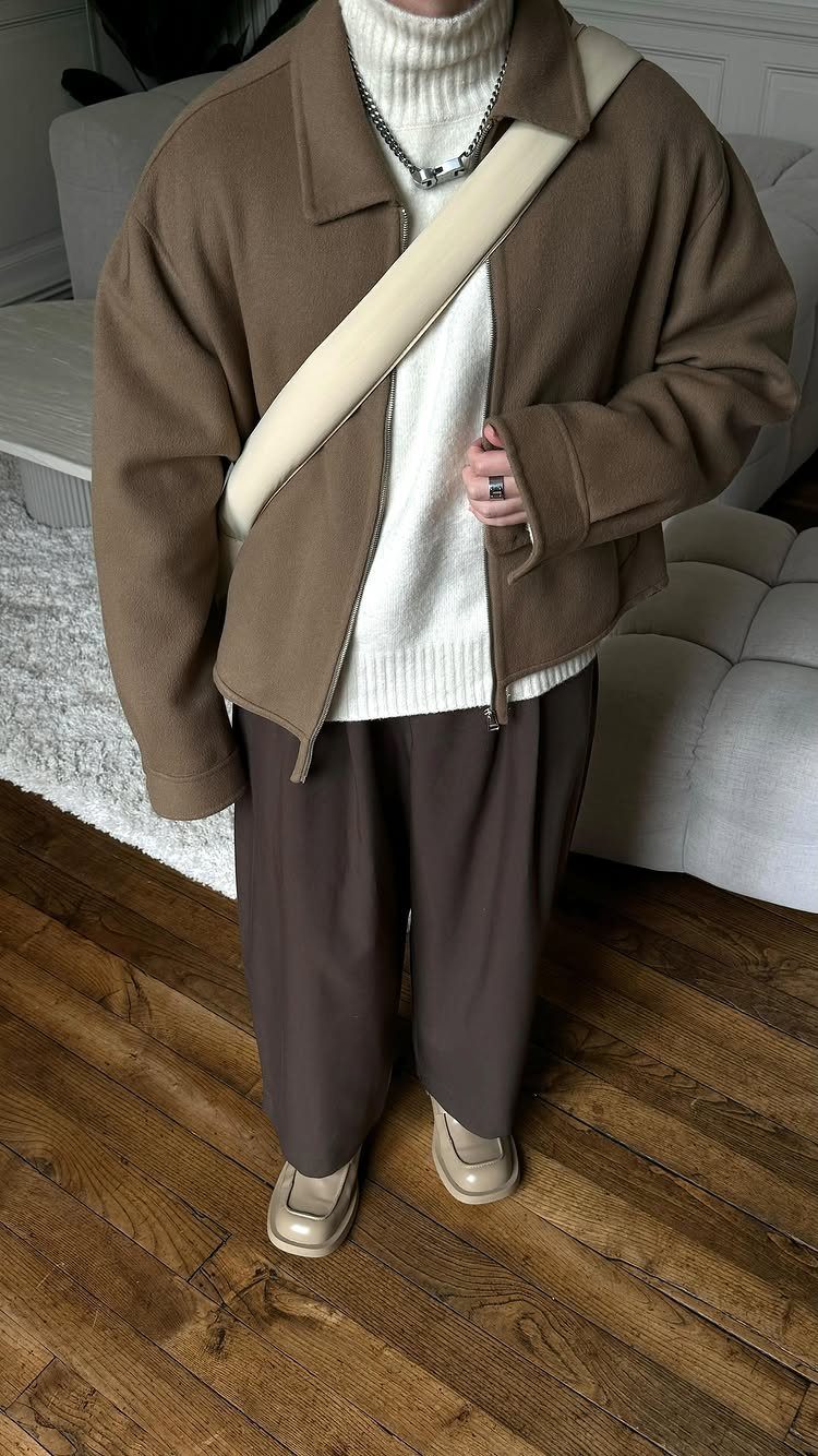 Person wearing a brown jacket over a white turtleneck and brown wide-leg trousers.