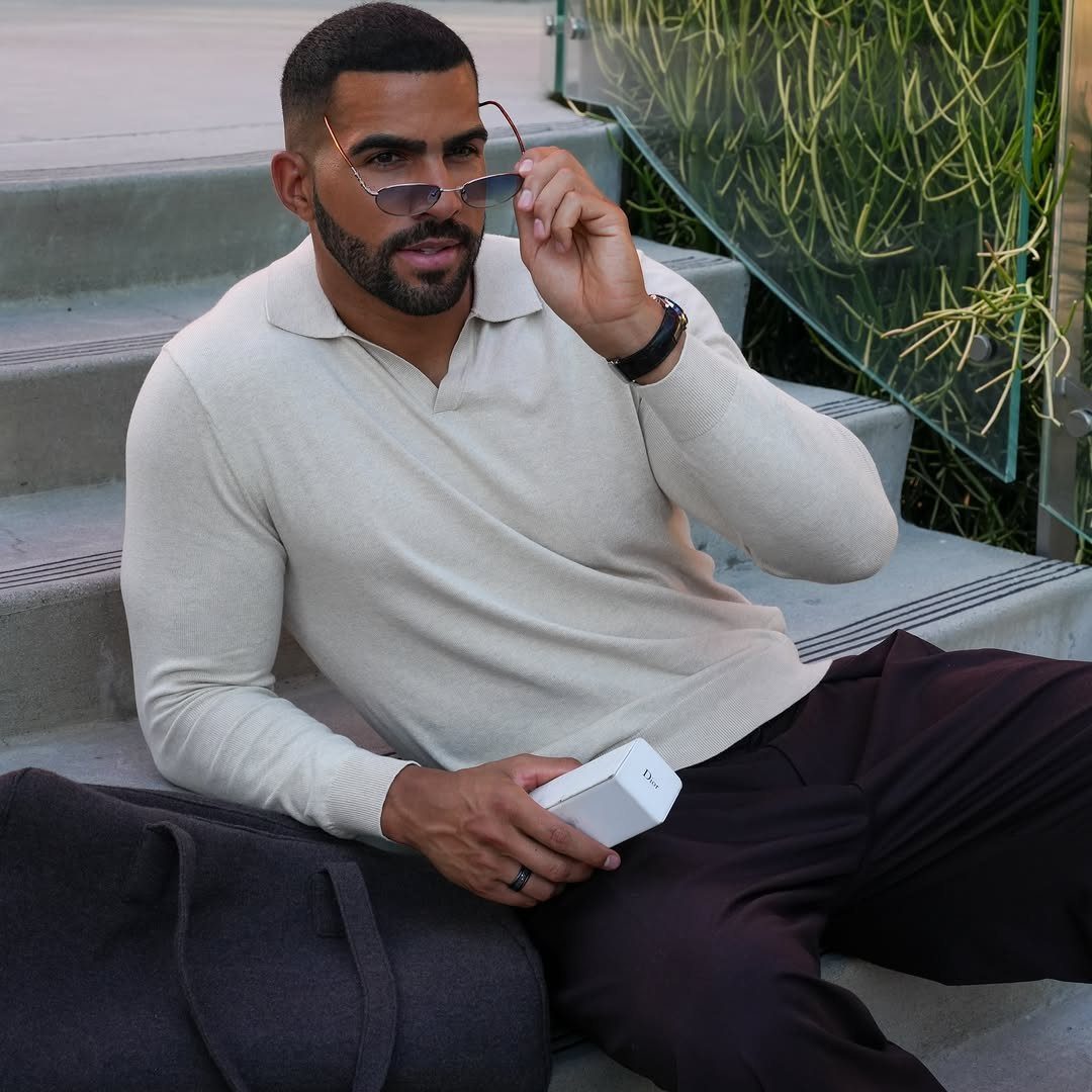 Man in cream long-sleeve polo and burgundy trousers sitting on concrete steps.