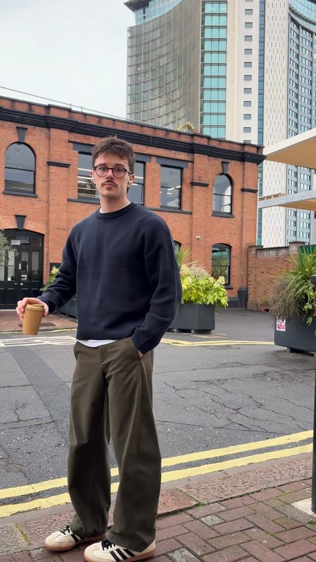 Man wearing a navy sweater and olive wide-leg trousers standing in a city street.