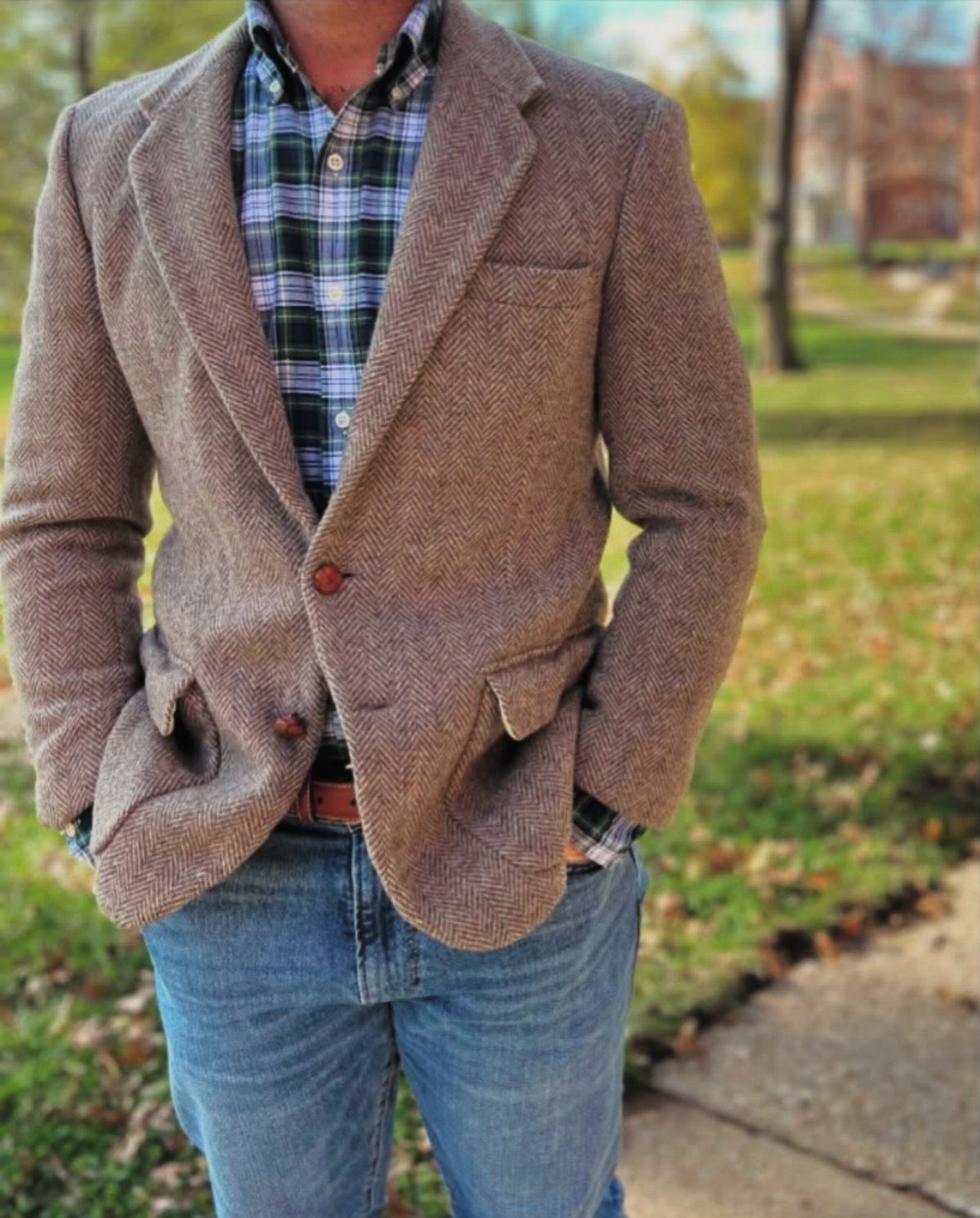 Man wearing a brown herringbone tweed sports jacket and plaid button-down shirt.