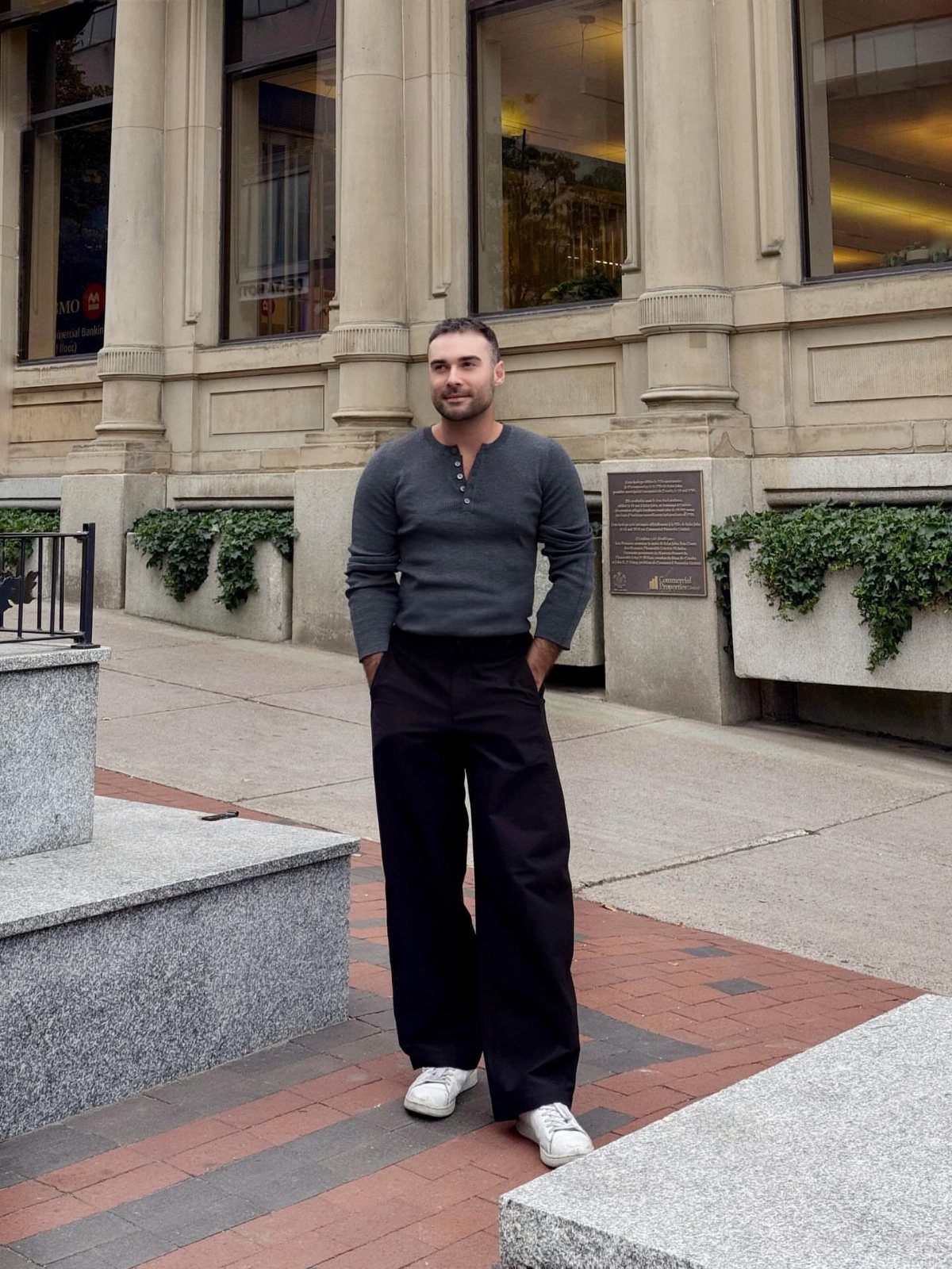 Man wearing a charcoal gray long sleeve henley shirt and wide black trousers.