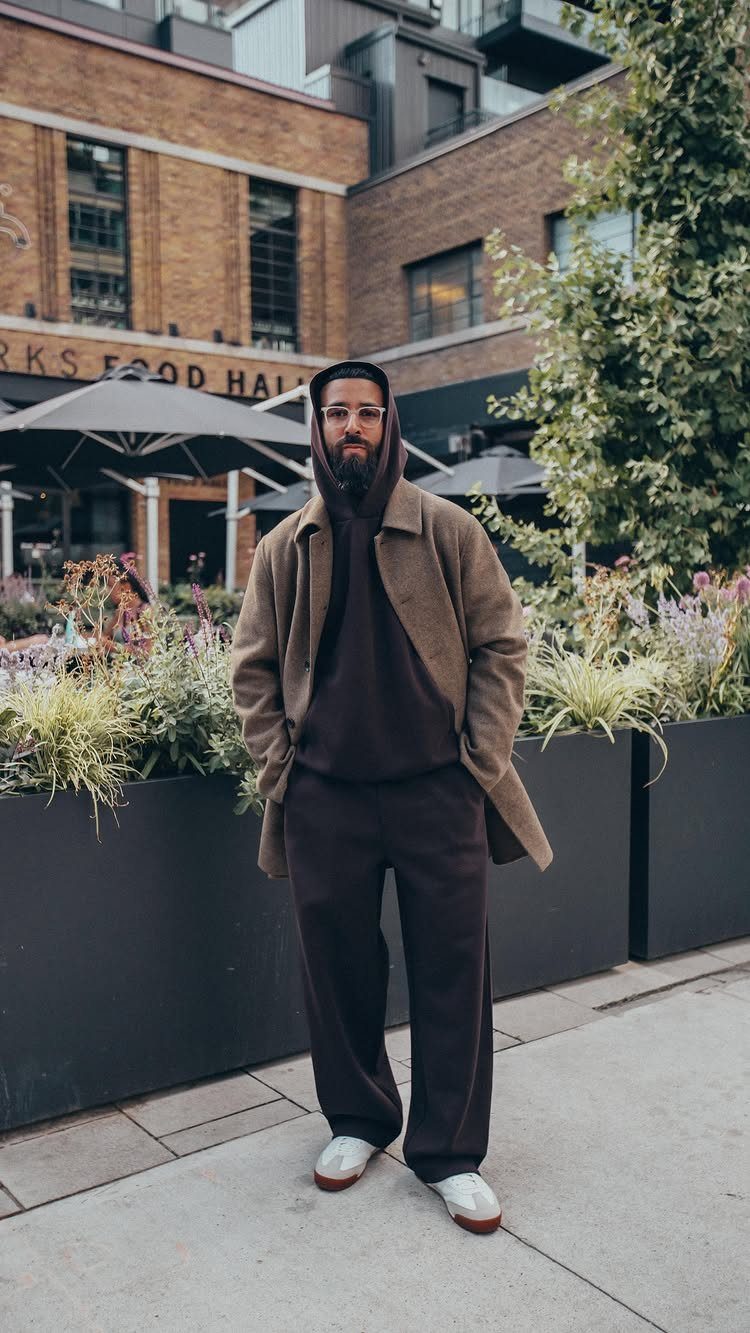 Man wearing a dark brown pullover hoodie under a tan overcoat and matching trousers.