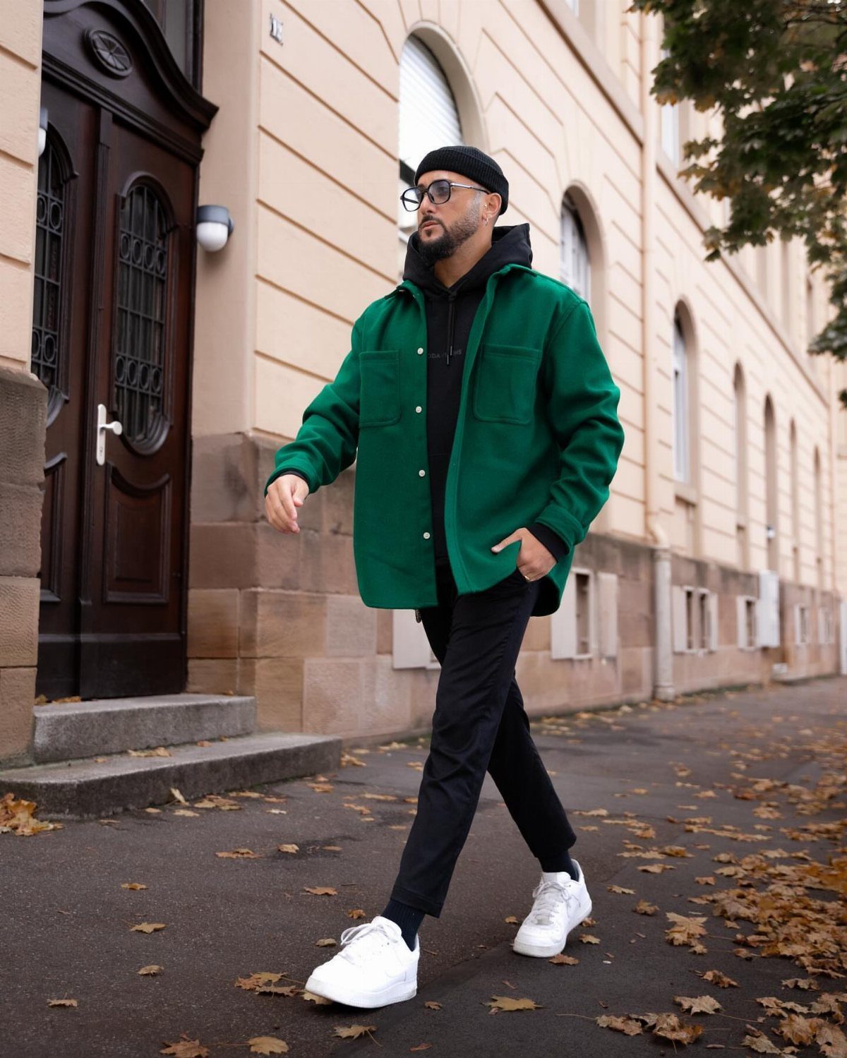 Man wearing a bright green jacket, black hoodie, and white sneakers walking outdoors.