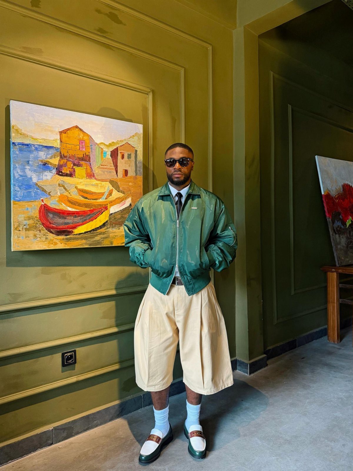 Man in green bomber jacket and beige wide-leg shorts standing in art gallery