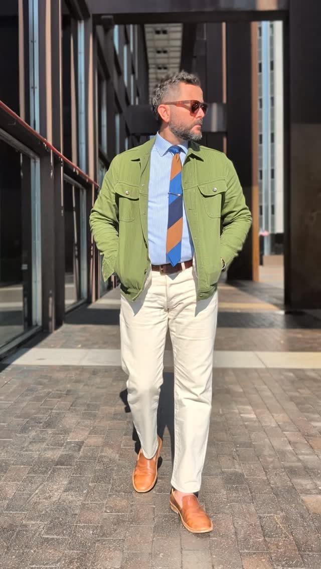 Man wearing a light green jacket, blue shirt, striped tie, and white trousers.