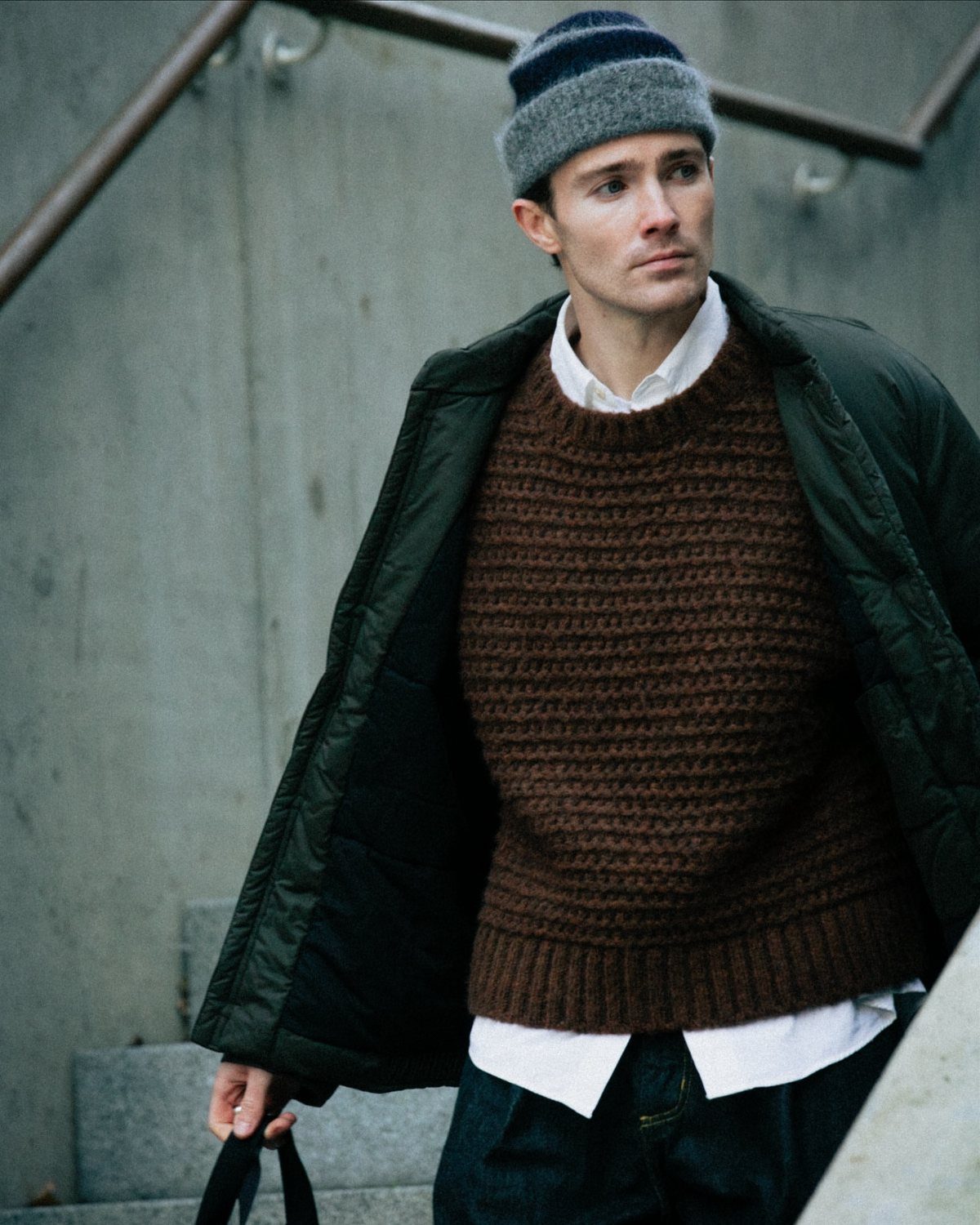 Man wearing a dark green quilted jacket, brown sweater, and a beanie.