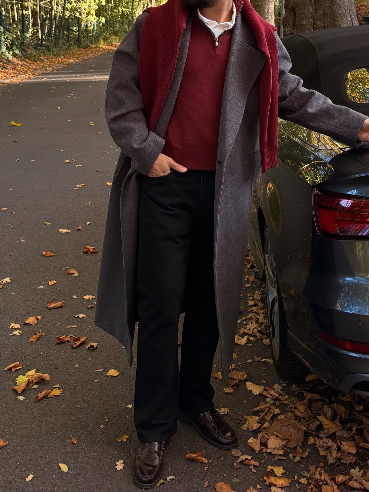 Person in a grey overcoat and burgundy scarf standing by a car.