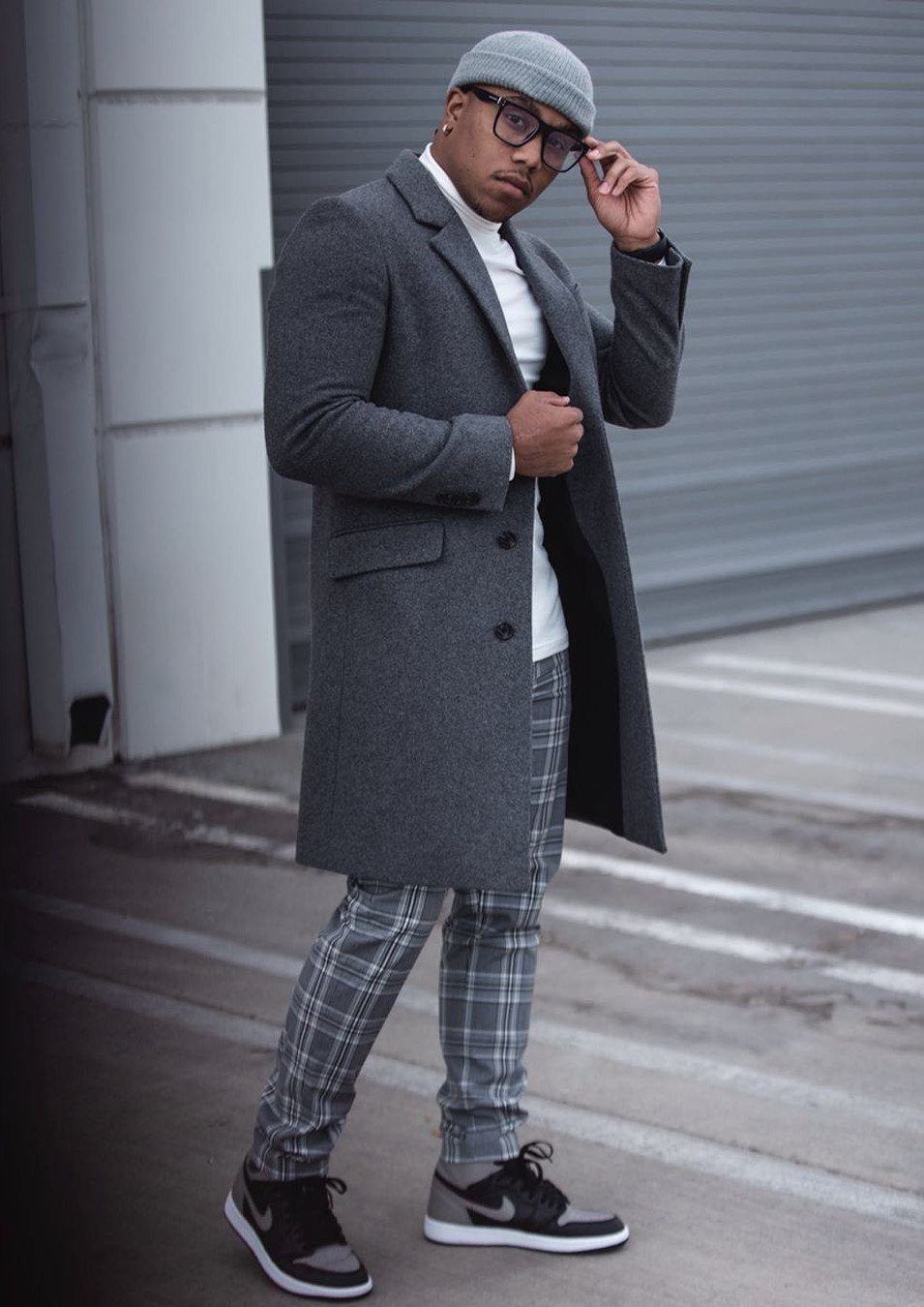 Man in grey overcoat and charcoal plaid dress pants with a white turtleneck.