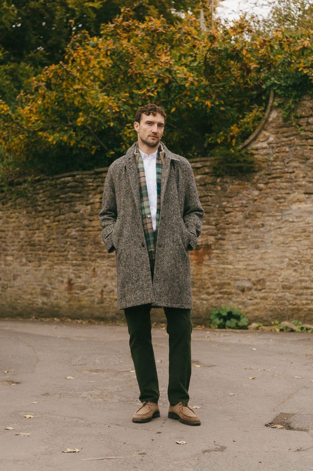 Man wearing a grey overcoat with olive chinos and brown leather shoes outdoors.