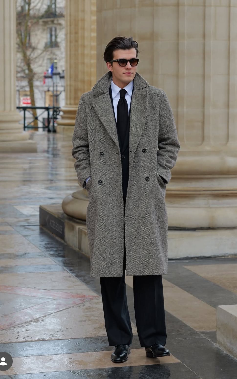 Man in a grey overcoat, white dress shirt, black tie, and black trousers.