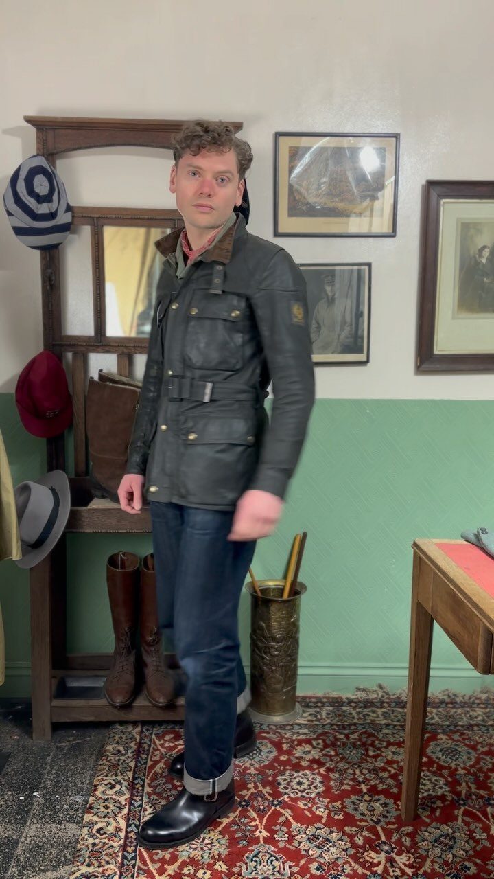 Man wearing a dark olive green waxed cotton field jacket and dark blue jeans.