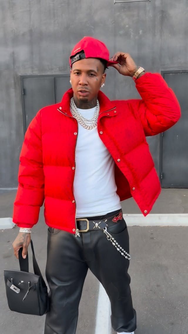 Man in red puffer jacket, red cap, and black leather pants posing outdoors.