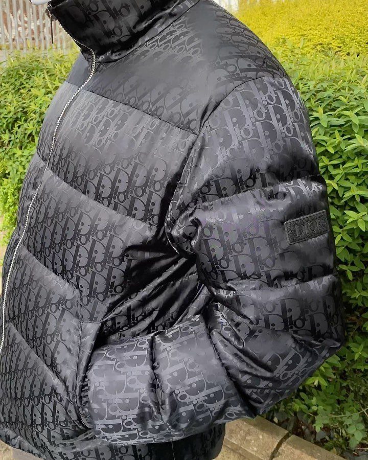 Black Dior monogram puffer jacket worn by a person against green foliage.