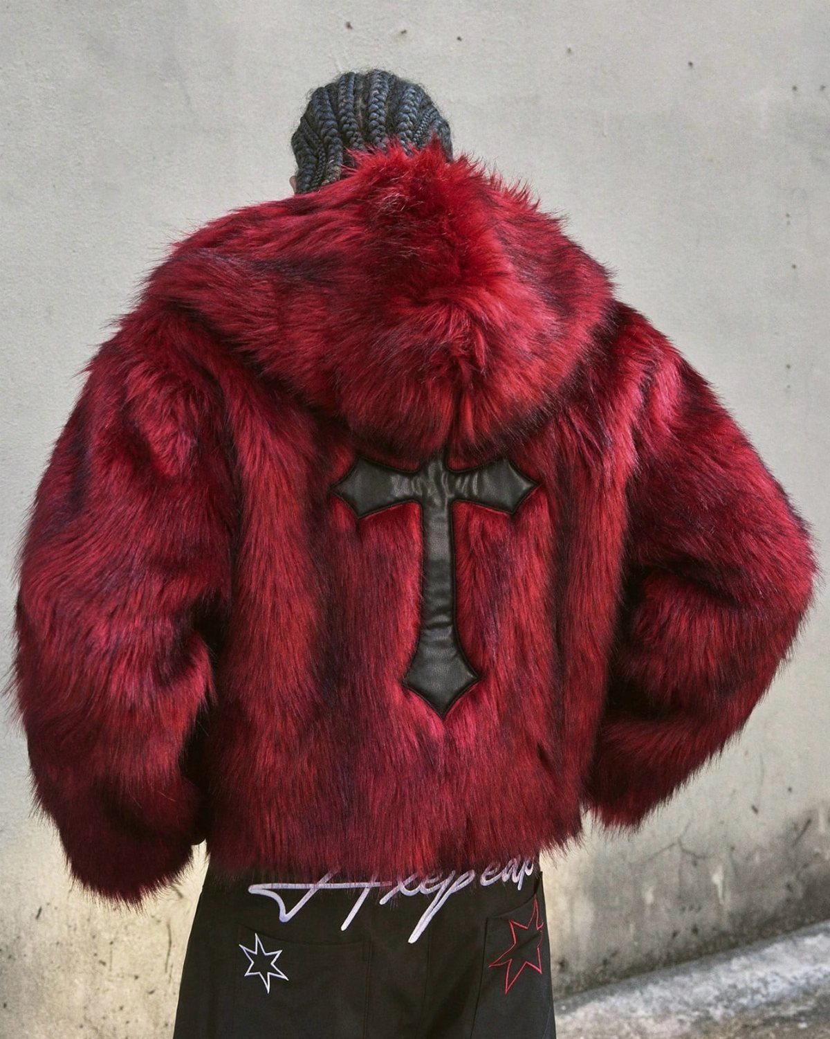 Person wearing a voluminous deep red fur coat with a black leather emblem.