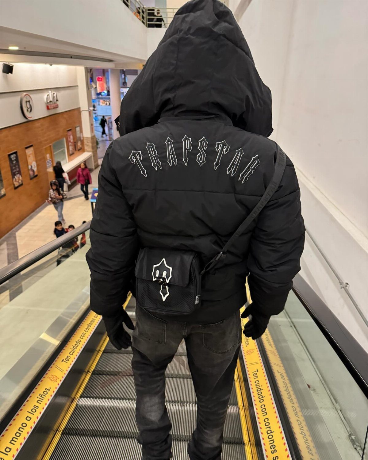 Person from behind wearing a black Trapstar puffer jacket on an escalator