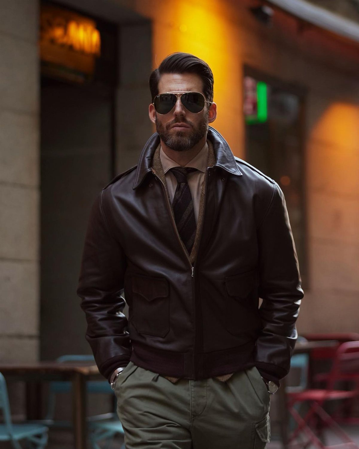 Man in brown leather jacket, tan shirt, tie, and olive green cargo pants.