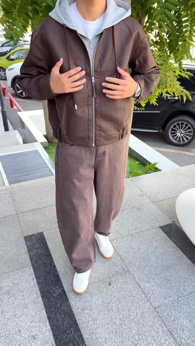 Person wearing a brown leather jacket over a grey hoodie and brown trousers.
