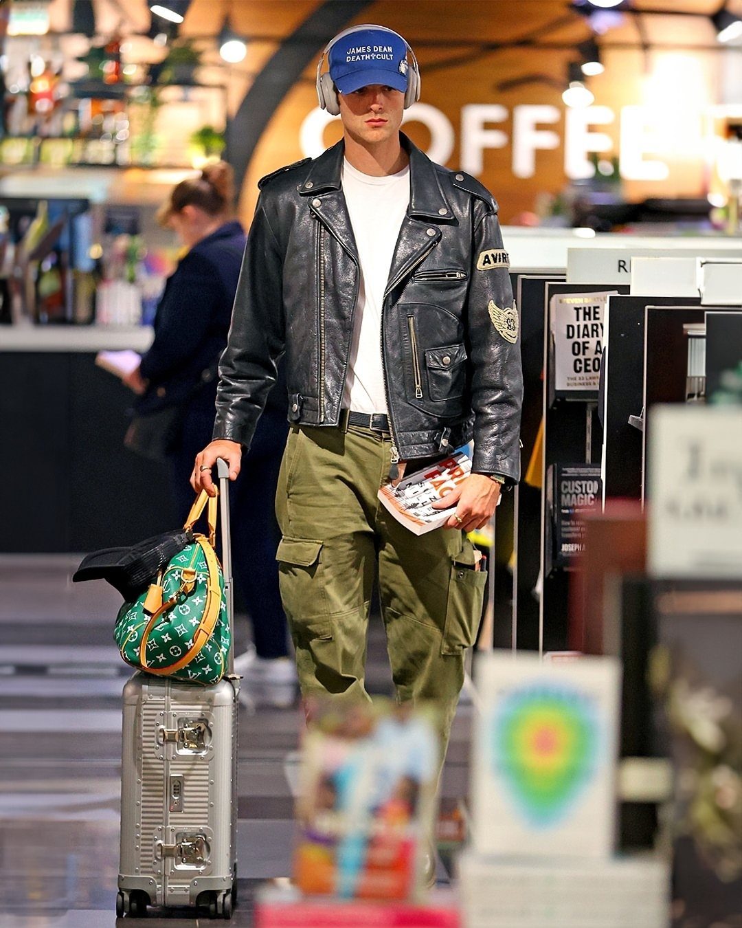 Man wearing a black leather jacket and olive green cargo pants with a suitcase