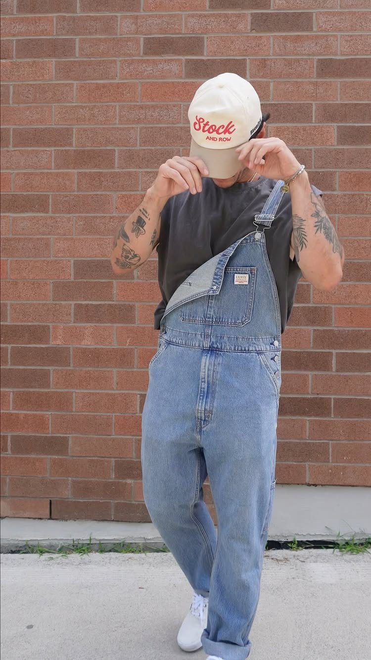 Person in blue denim overalls with one strap down and a white cap.