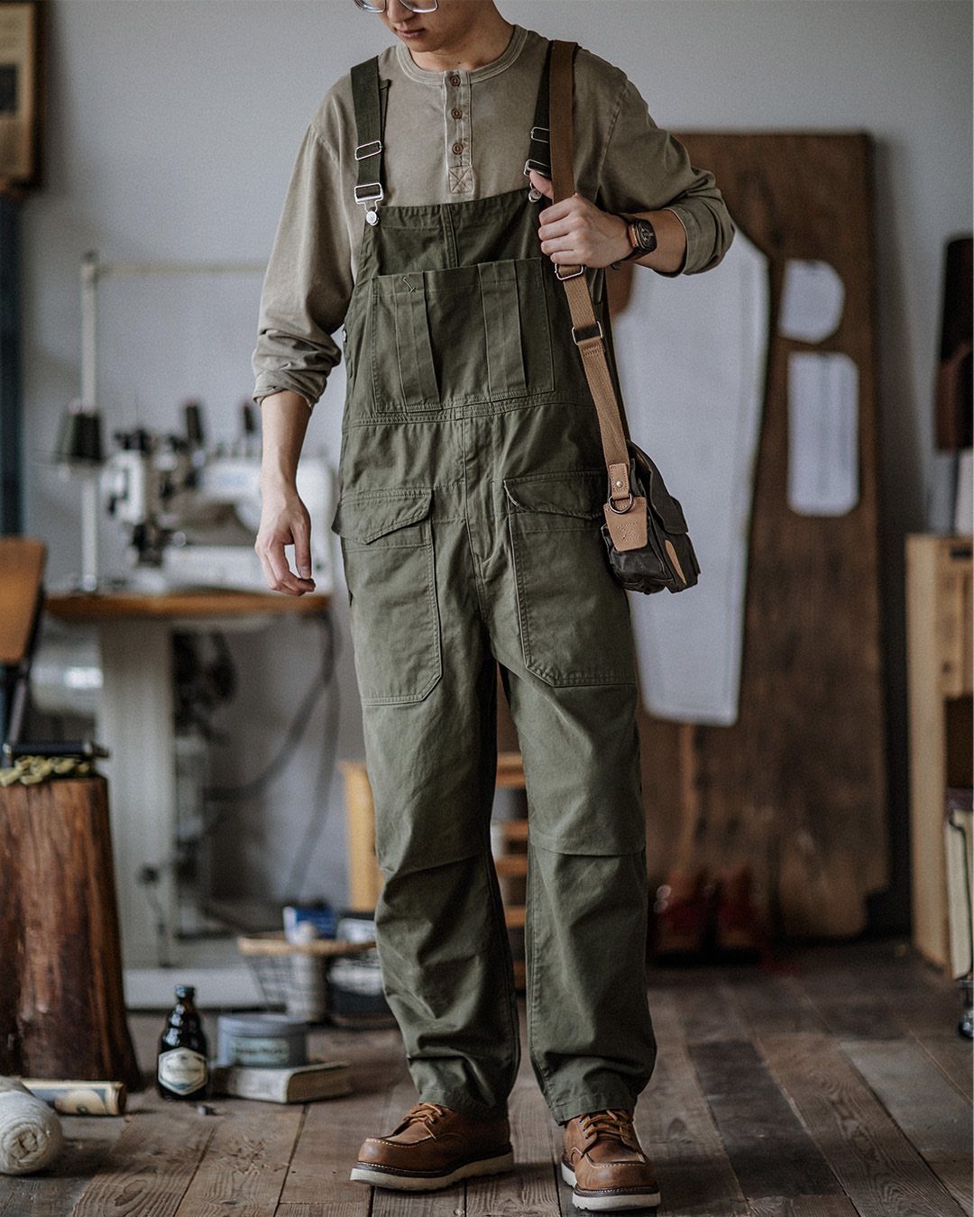 Person wearing olive green overalls and brown leather shoes in a workshop setting.