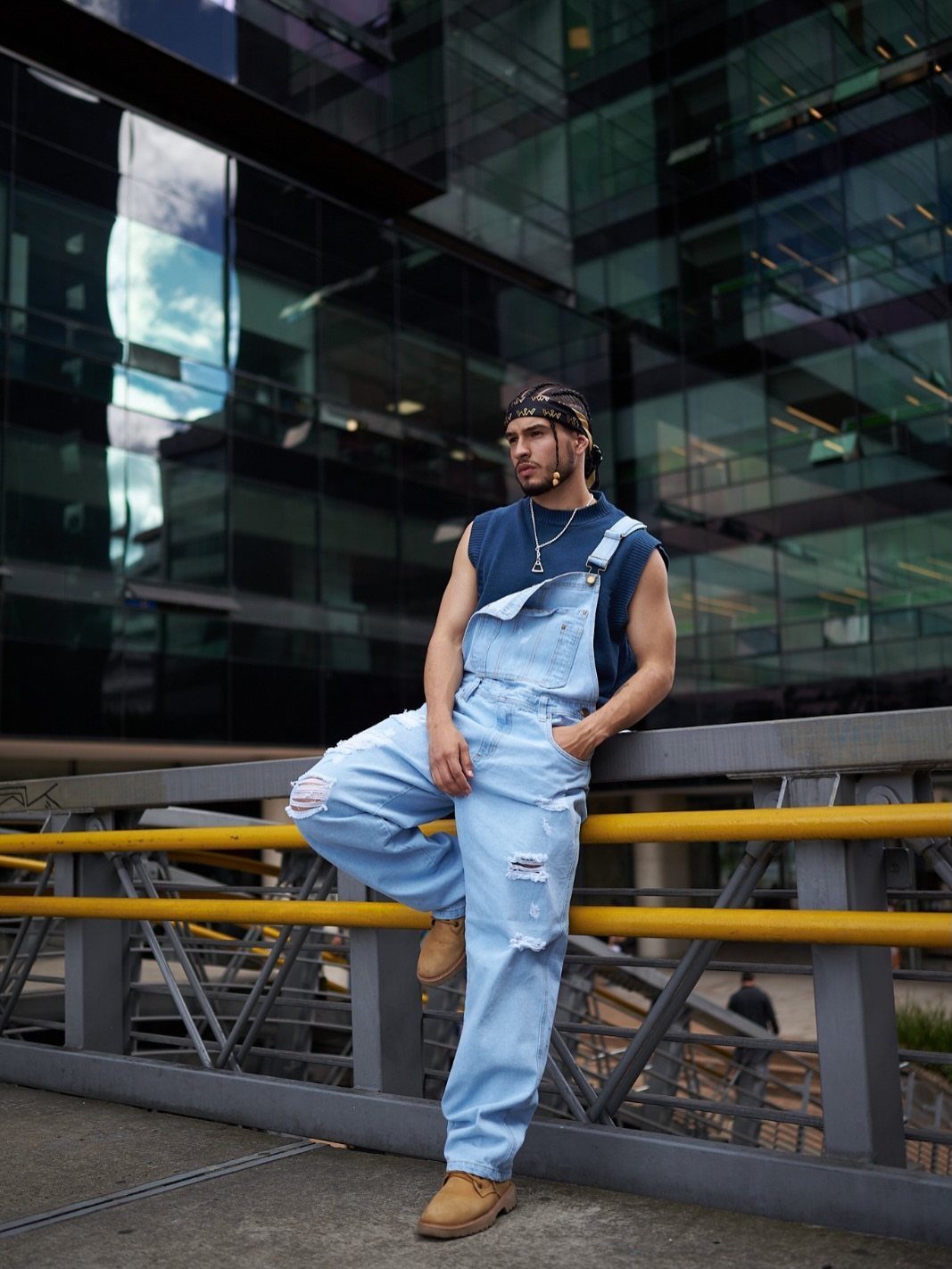 Man in light blue denim overalls and a plain dark blue top leaning on railing