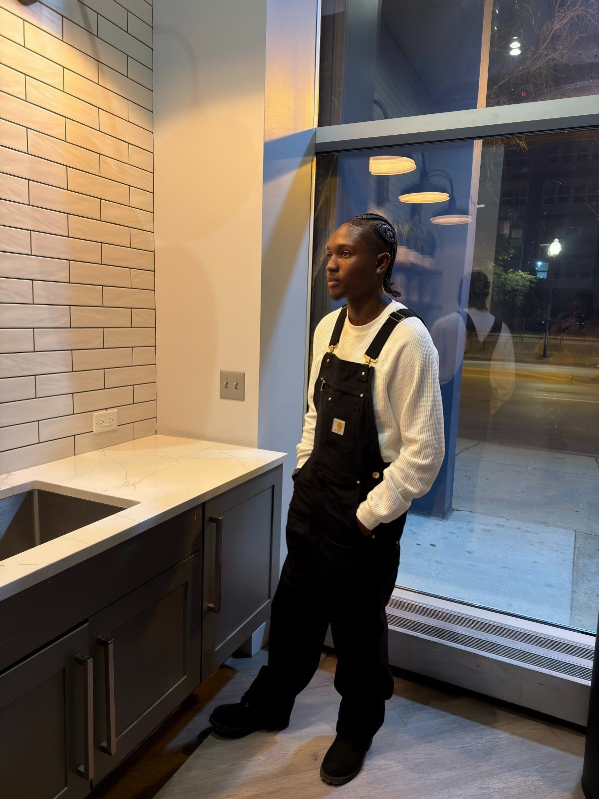 Person wearing black overalls and a white ribbed sweater in a modern kitchen.