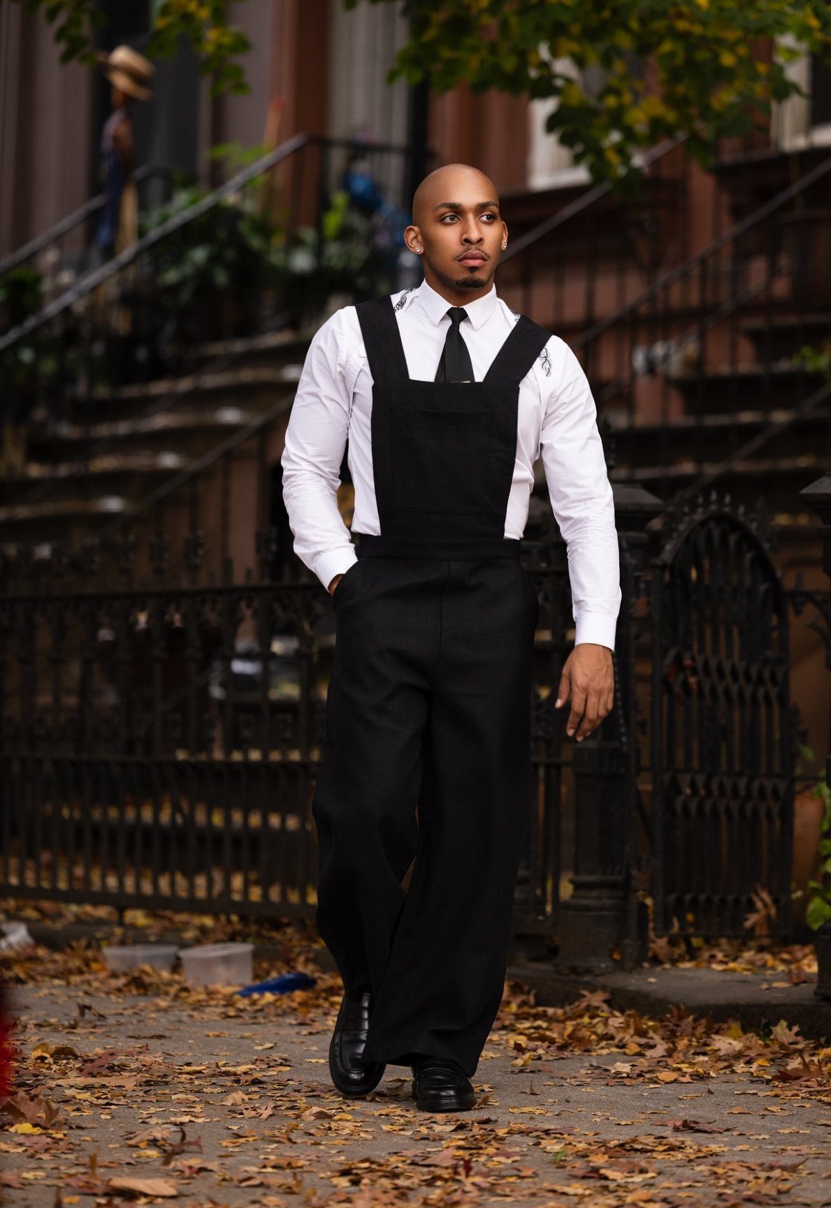 Man wearing black overalls with a white button-up shirt and black tie.