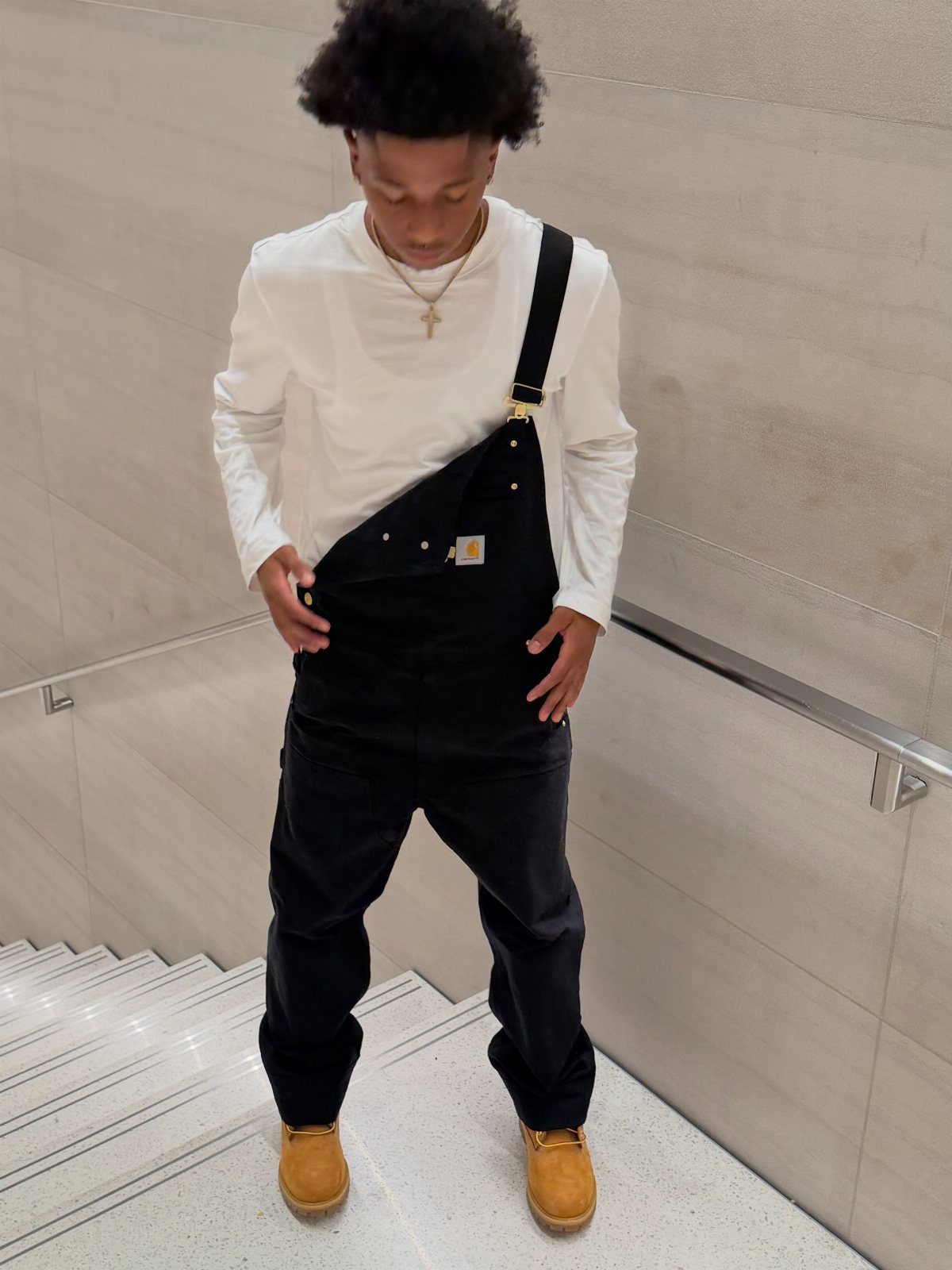 Man in black overalls with one strap loose, white shirt, and tan boots.
