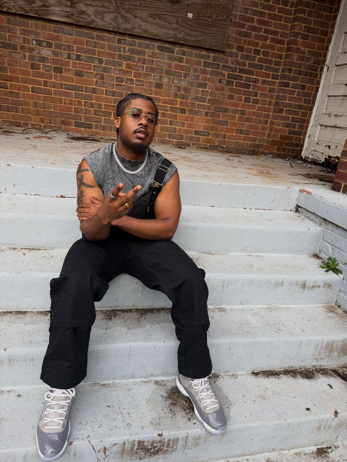 Man in black overalls and grey sleeveless tee wearing grey sneakers on steps