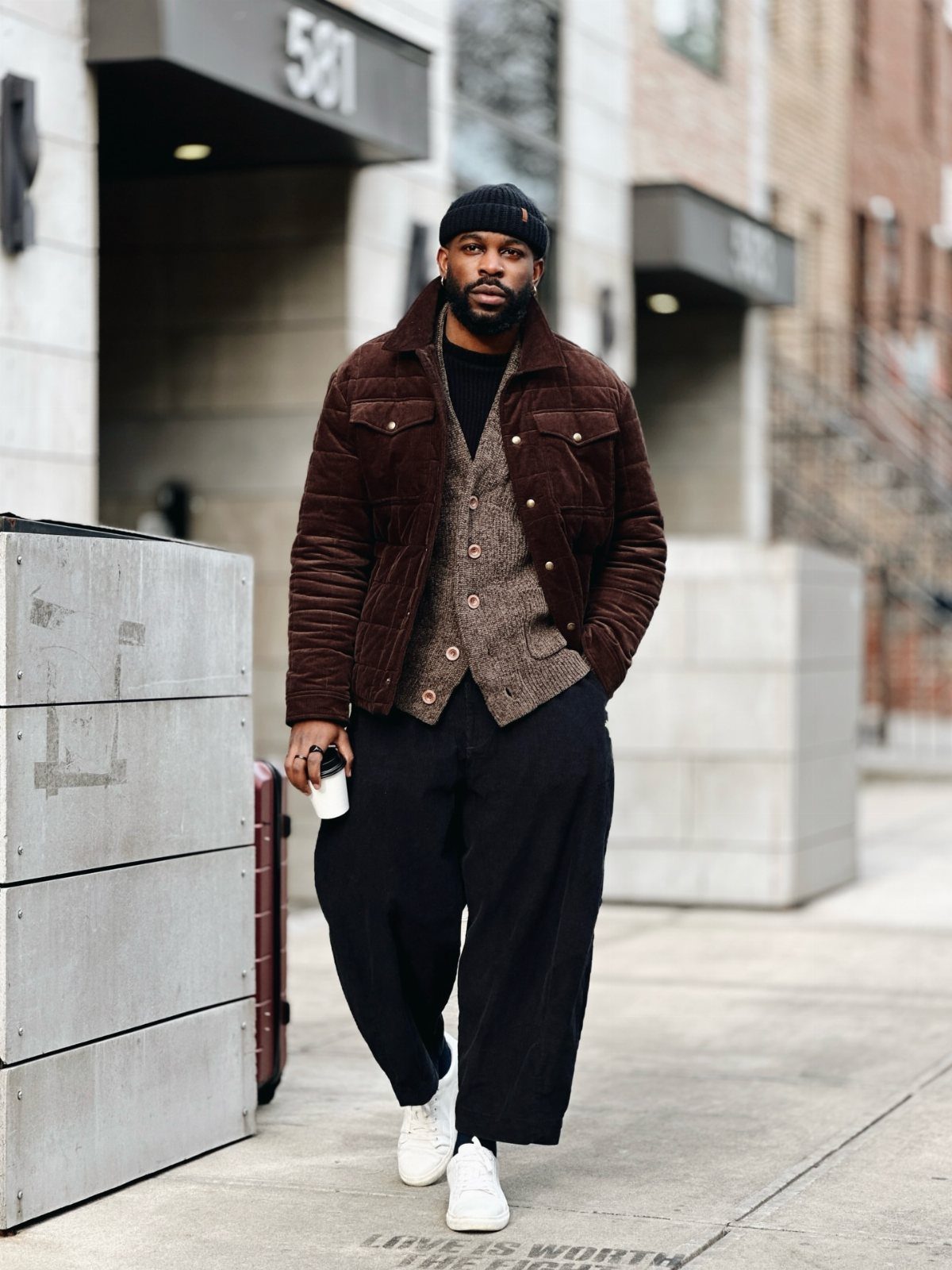 Man in brown corduroy jacket and black wide-leg trousers on a city street