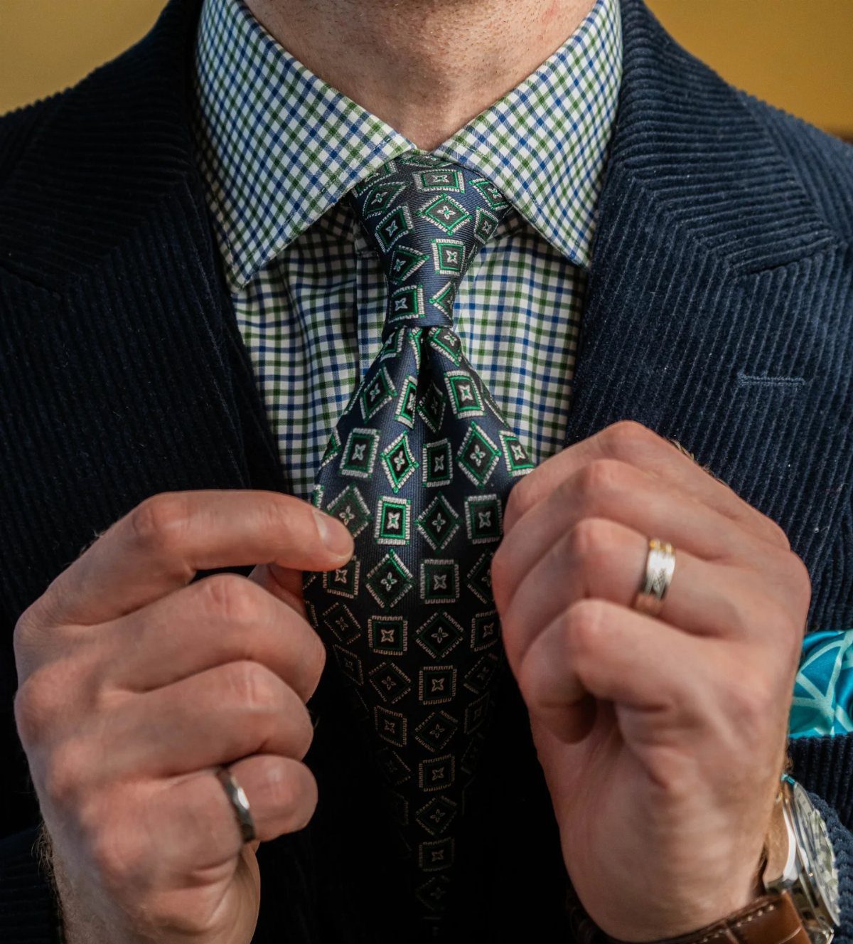 Man wearing a dark blue corduroy jacket with a checkered shirt and patterned tie.