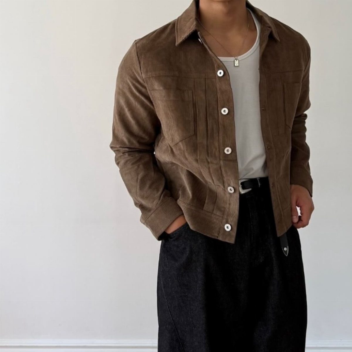 Person wearing a brown corduroy jacket over a white t-shirt and black pants.