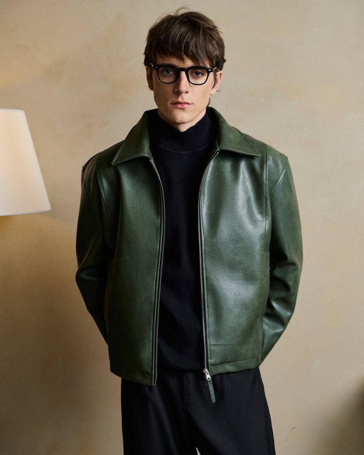 Man wearing a dark green leather jacket over a black turtleneck and glasses.