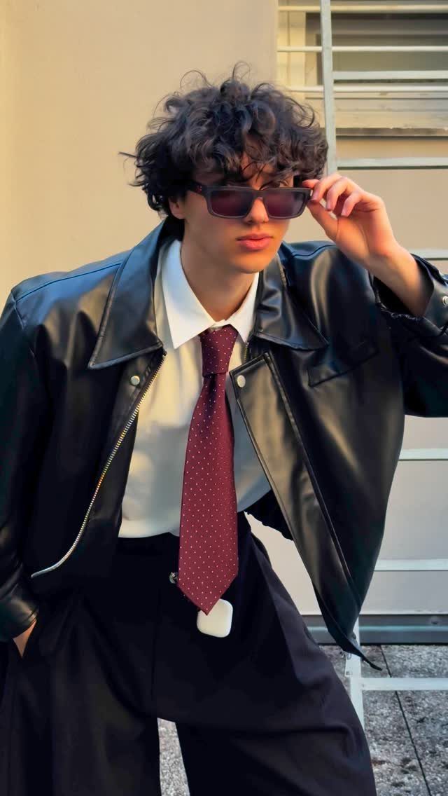 Young man wearing a black leather jacket, white shirt, and red polka-dot tie.