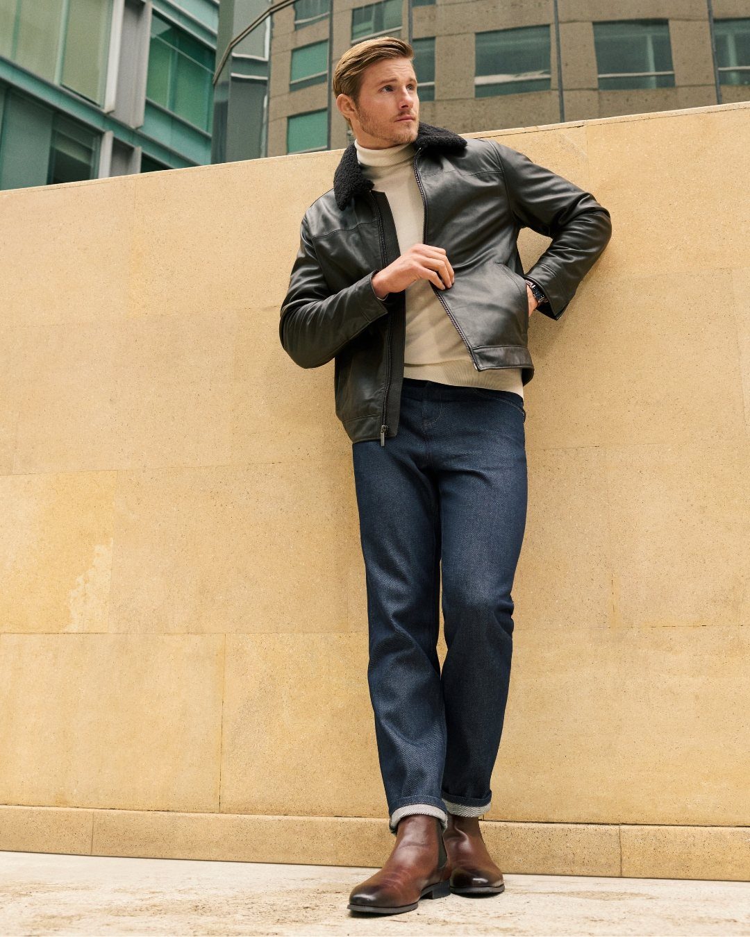Man wearing a black leather jacket with shearling collar and cream turtleneck sweater.
