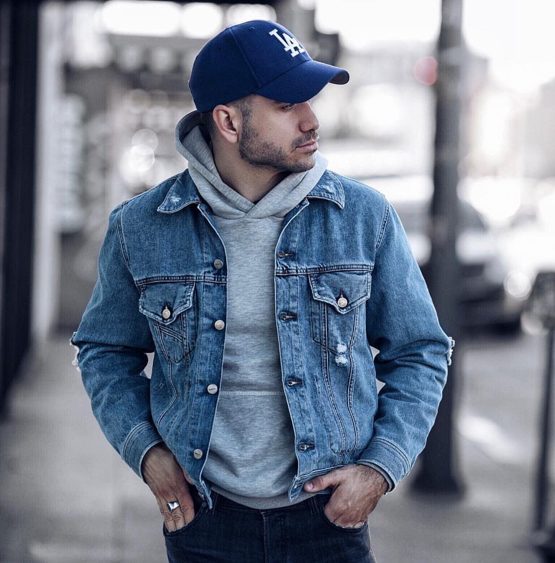 Man wearing a blue denim jacket over a grey hoodie and blue cap.