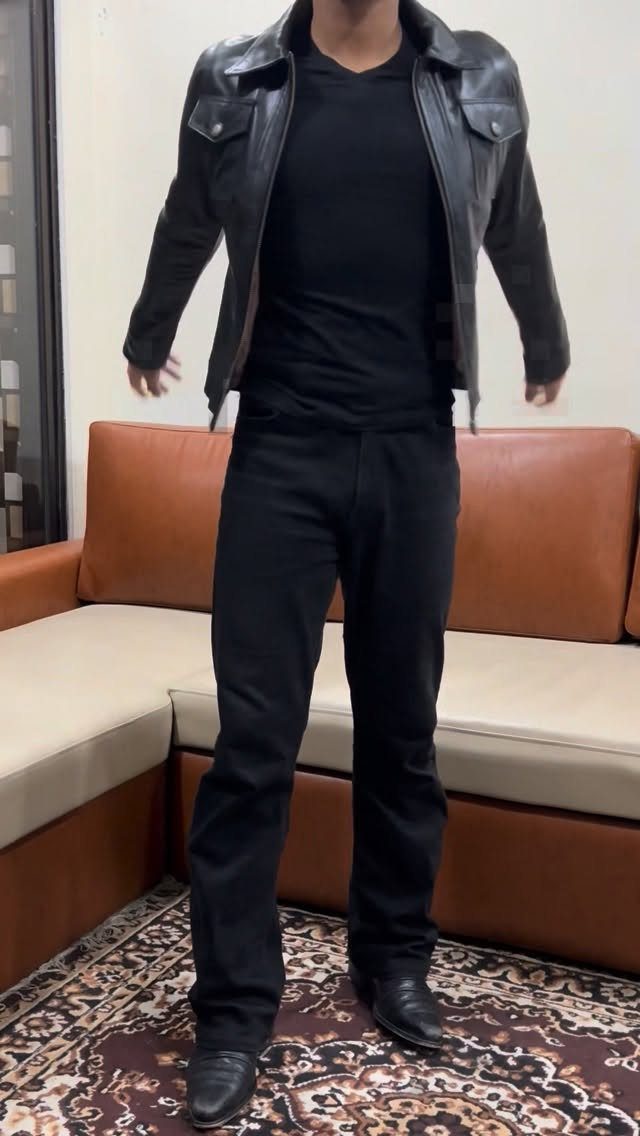 Person wearing a black leather jacket, black t-shirt, and black jeans standing indoors.